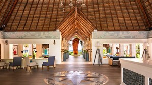 A spacious lobby with a high thatched ceiling, a central art installation, and a floor with a compass design.