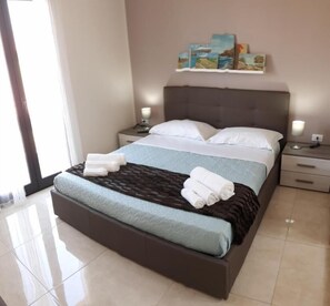 A modern hotel room with a large bed, two bedside tables, and a view of the outdoors. - Antares B&B (Comiso)