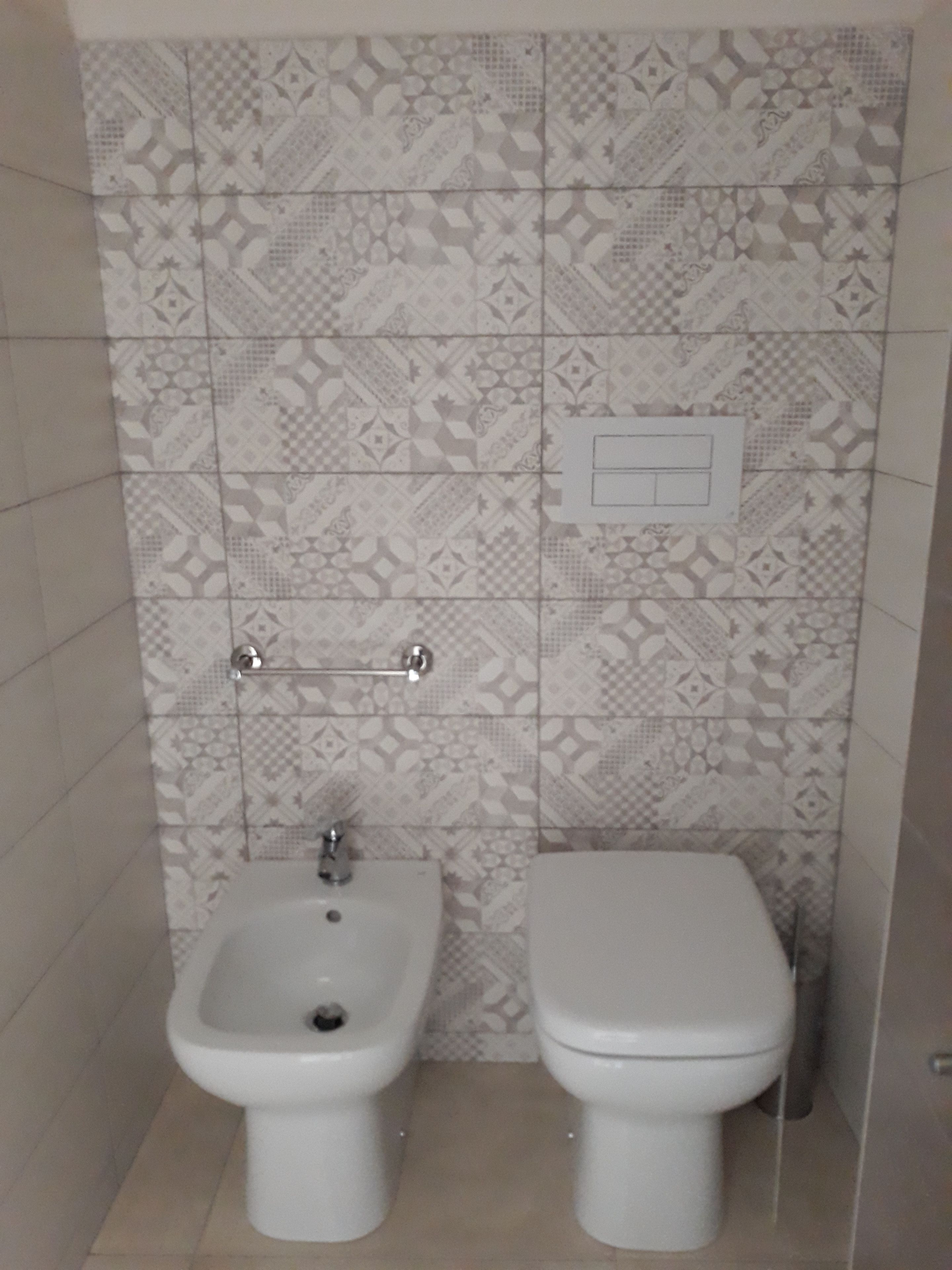 Un baño con bidé, inodoro y baldosas estampadas.