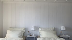 Habitació amb dos llits, cadascun amb capçal blanc i almoines a joc. Hi ha dues taules rodones petites amb làmpades i ampolles de vidre a sobre.