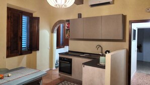A compact kitchen with a built-in oven, a sink, and a countertop. There is a window with wooden shutters and a pendant light above the counter. - Carducci bright flat in historic centre (Pistoia)