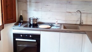 A compact kitchen with a dishwasher, a stove, a sink, and a wooden backsplash. - Carducci bright flat in historic centre (Pistoia)