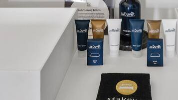 Un tocador de baño con una toalla negra para maquillaje, varios productos de crema y jabón DuVet, y un espejo con marco dorado.