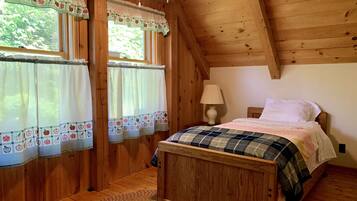 A wooden cabin bedroom with a bed, a nightstand, a lamp, and curtains with fruit patterns.