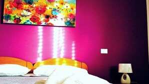 A hotel room with a bed, pillows, a bedside lamp, and a colorful painting on the wall. - B&B Federico II (San Cipirello)