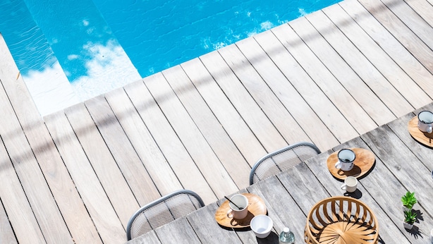 Eine Holzterrasse mit Pool, Sitzgelegenheit und einem Tisch mit Tassen und einer Flasche.