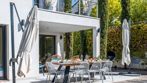 Ein moderner Außenbereich mit Essplatz, Pool, Holzterrasse und Kübelpflanzen.