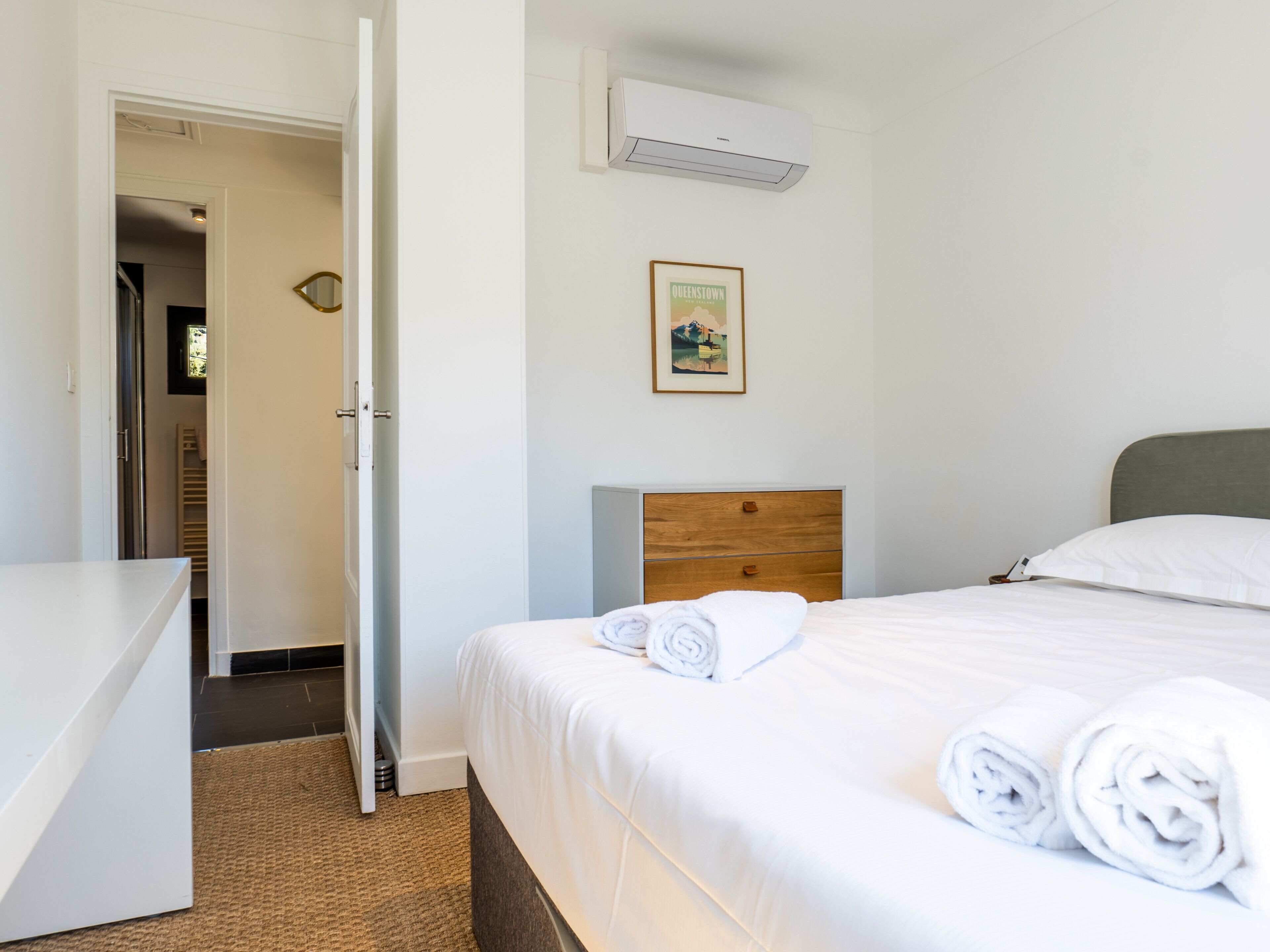 Et hotelværelse med en seng, et trænatbord, en hvid kommode og en aircondition på væggen.