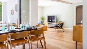 Ein moderner Essbereich mit einem Holztisch, gedeckt für vier Personen, einem Fernseher im Hintergrund und einem großen Fenster, das natürliches Licht hereinlässt.