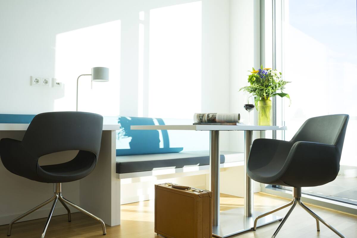 A modern room with two black chairs, a small table, a vase with flowers, and a suitcase on the floor.