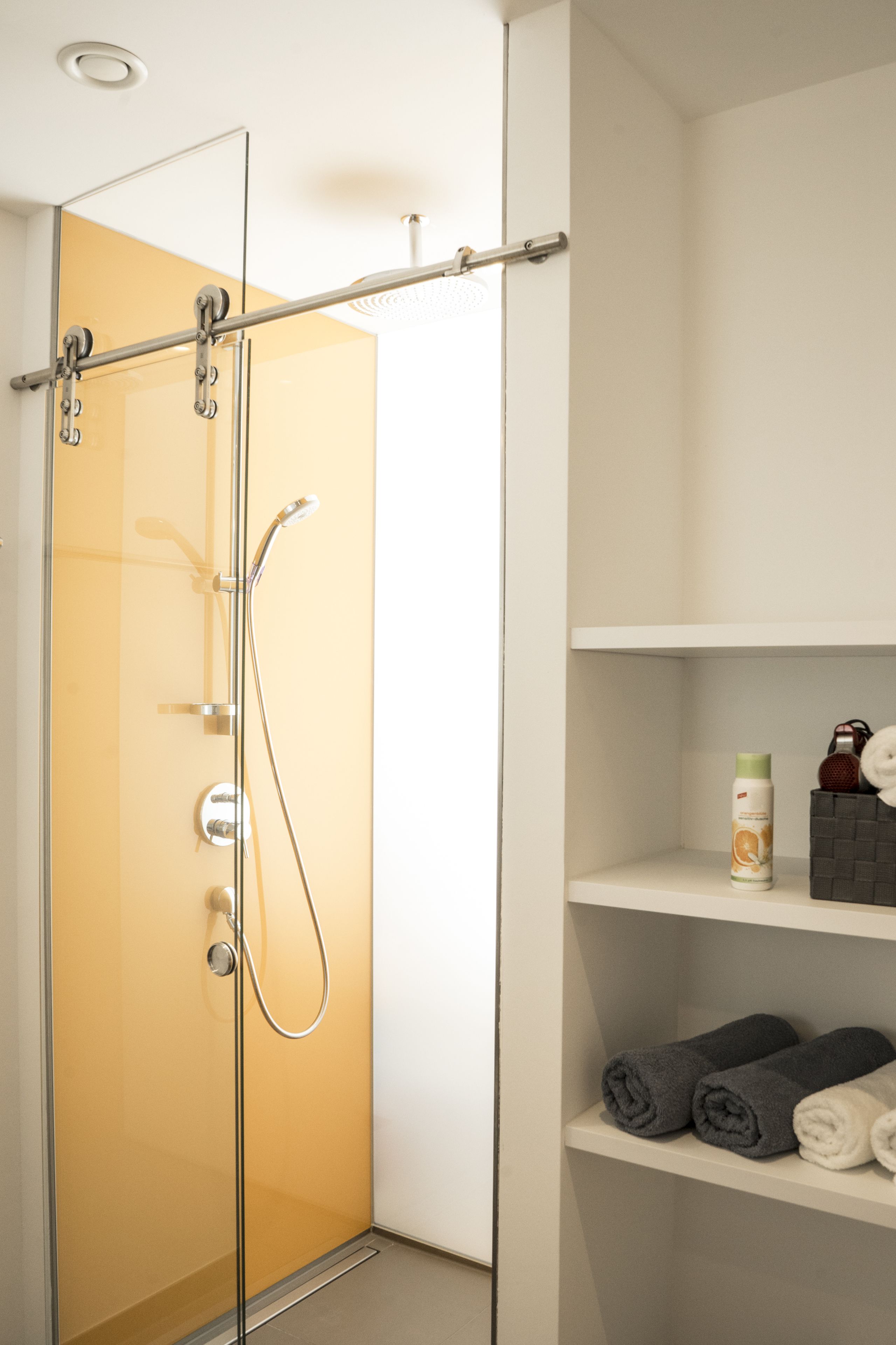 Un baño moderno con cabina de ducha de vidrio, tocador blanco con estantes y toallas dobladas cuidadosamente.