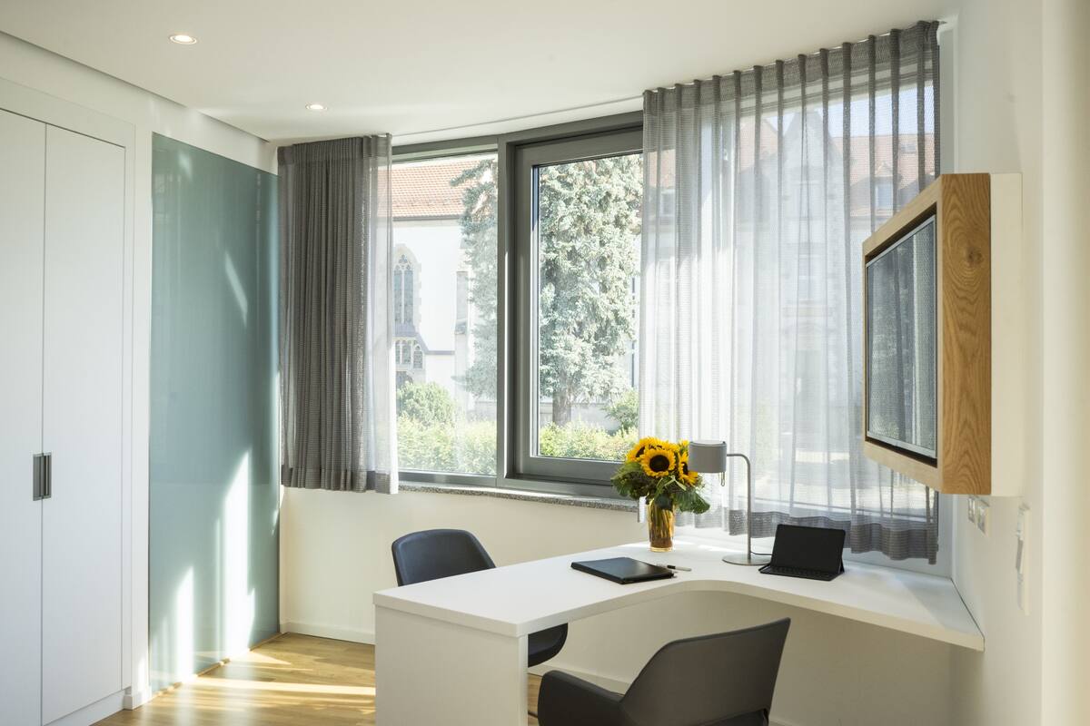 A modern room with a white desk, two chairs, a laptop, a tablet, and a vase with sunflowers.