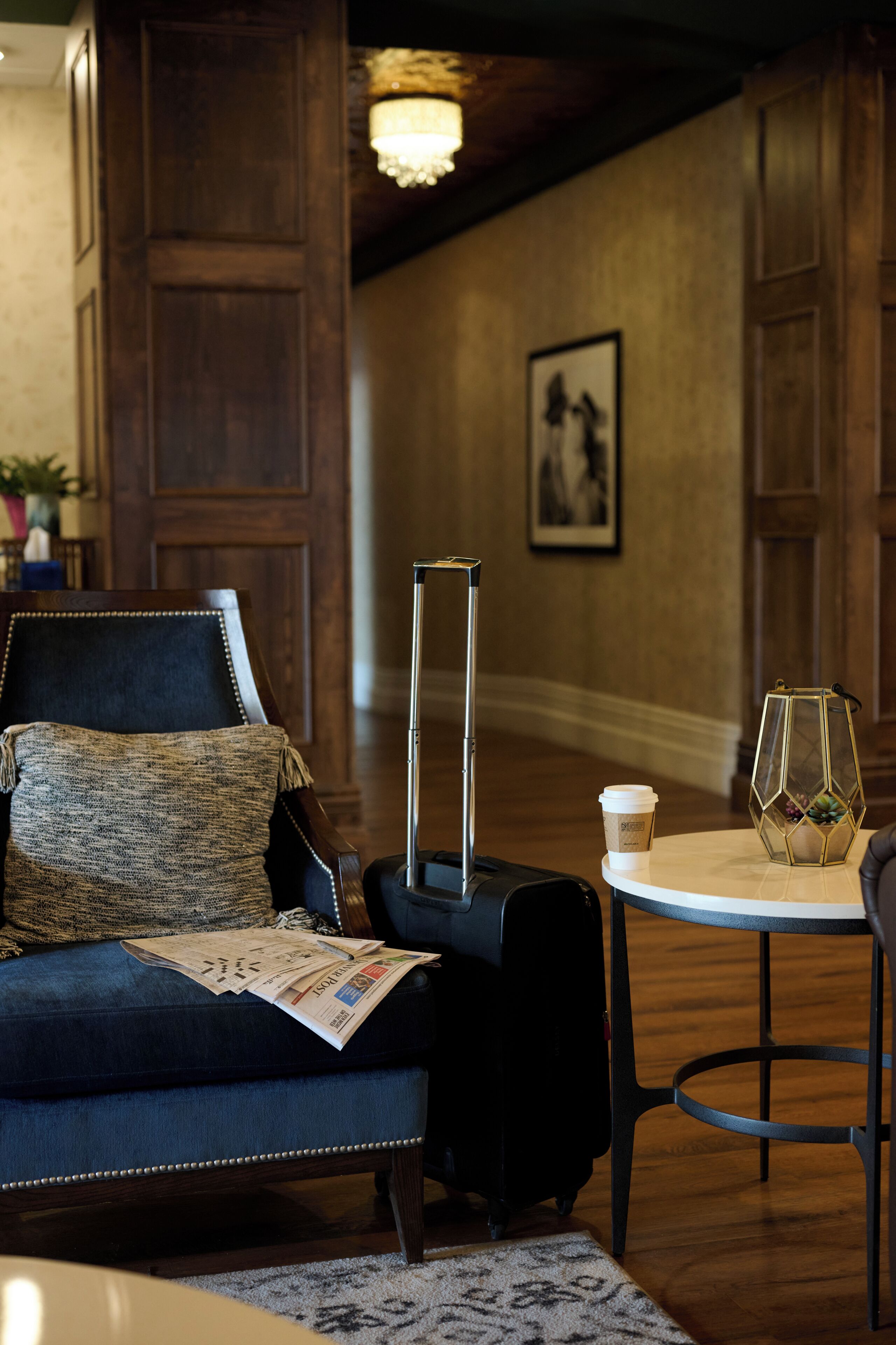A hotel room with a dark blue sofa, a small table with a glass and a coffee cup, and a suitcase.