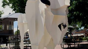 Una escultura abstracta blanca en un entorno exterior, con árboles y un edificio al fondo.