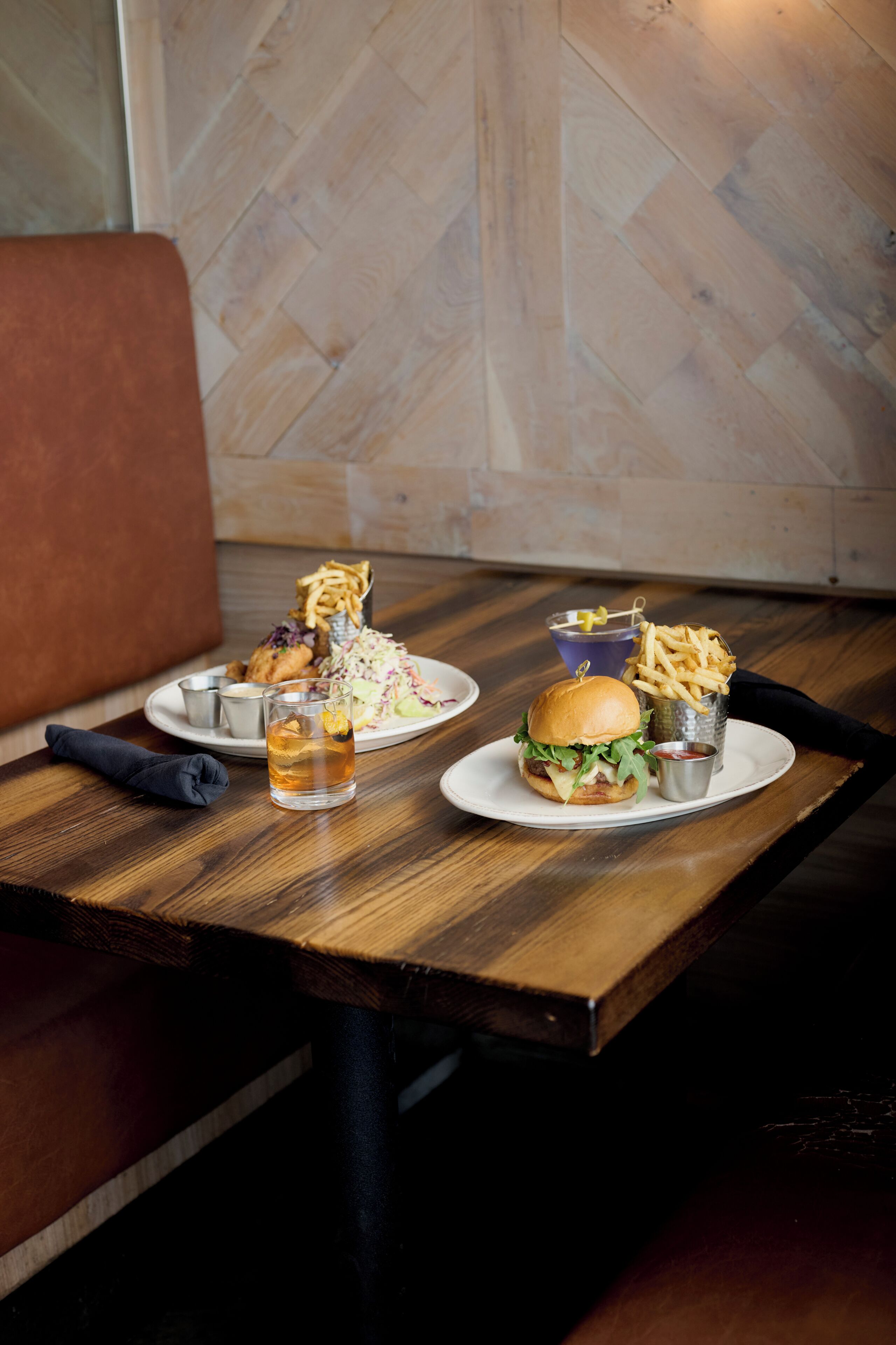 A dining table with a burger, fries, coleslaw, and a drink.