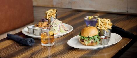 A dining table with a burger, fries, coleslaw, and a drink.