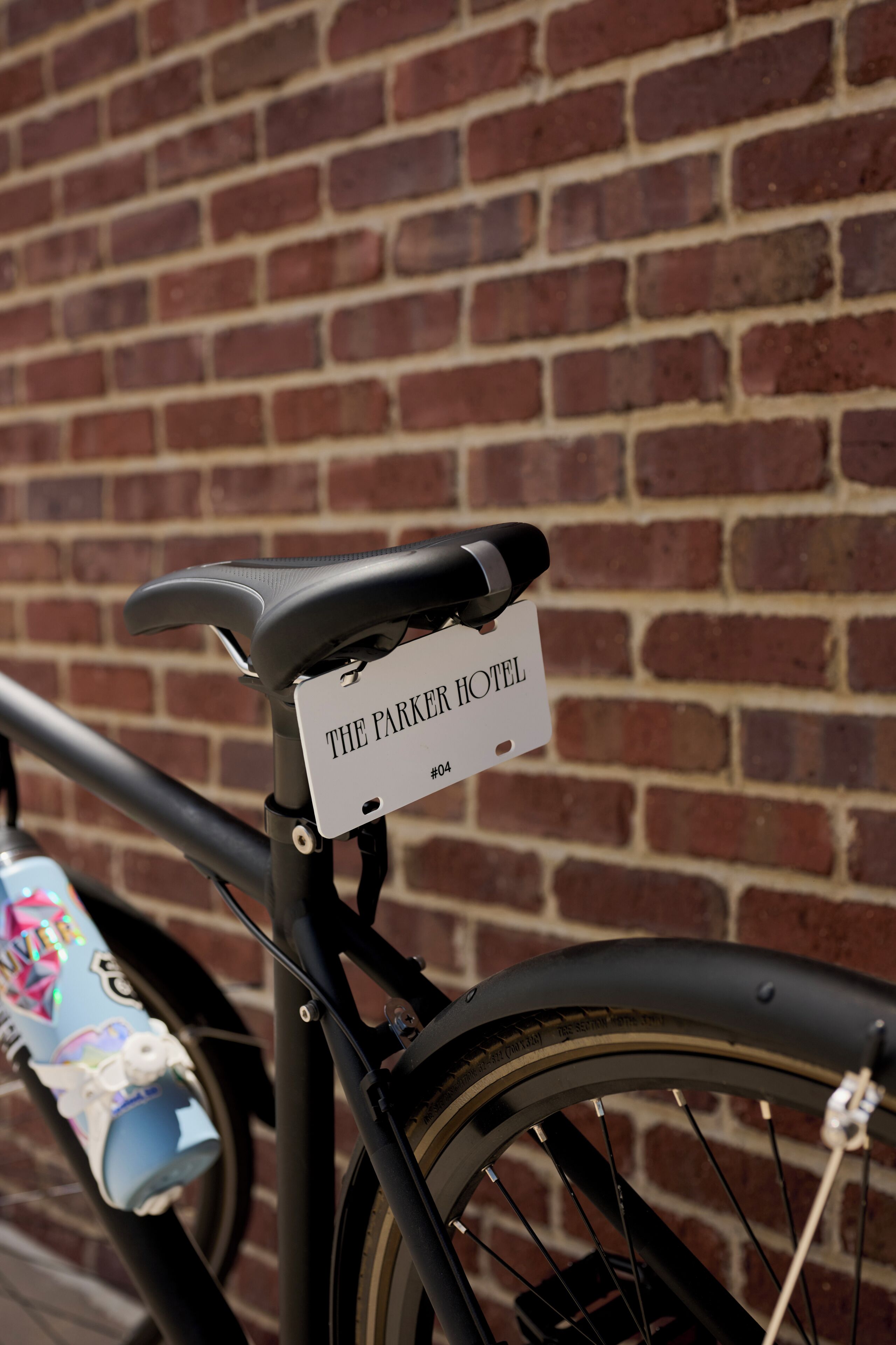 A bicycle with a sign attached to the frame that reads 'THE PARKER HOTEL #04'.