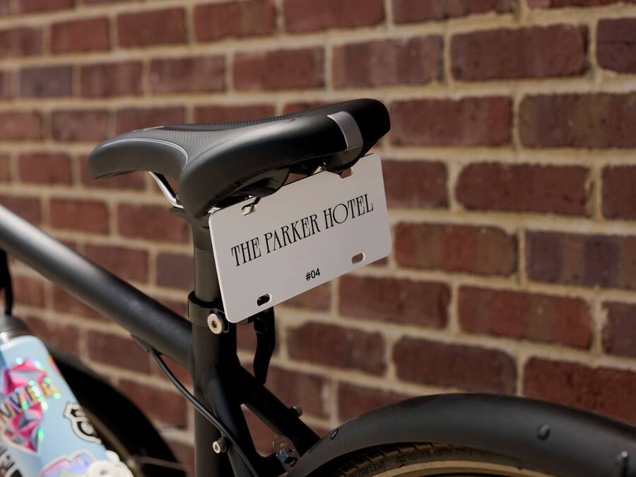 A bicycle with a sign attached to the frame that reads 'THE PARKER HOTEL #04'.