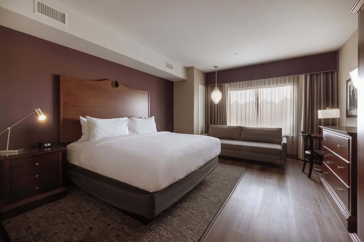 A hotel room with a large bed, a sofa, a dresser, and a desk with a lamp.