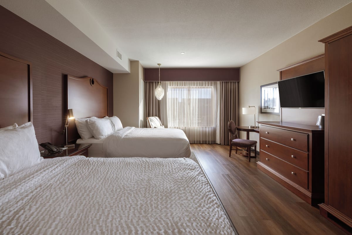 A hotel room with two beds, a TV, a dresser, and a desk with a chair.