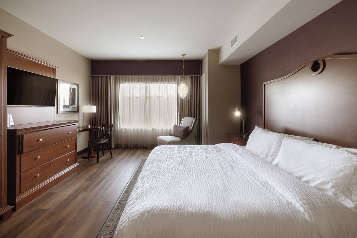 A hotel room with a large bed, a desk with a chair, a TV, and a window with curtains.