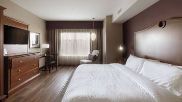 Habitación de hotel con una cama grande, un escritorio con silla, televisión y ventana con cortinas.