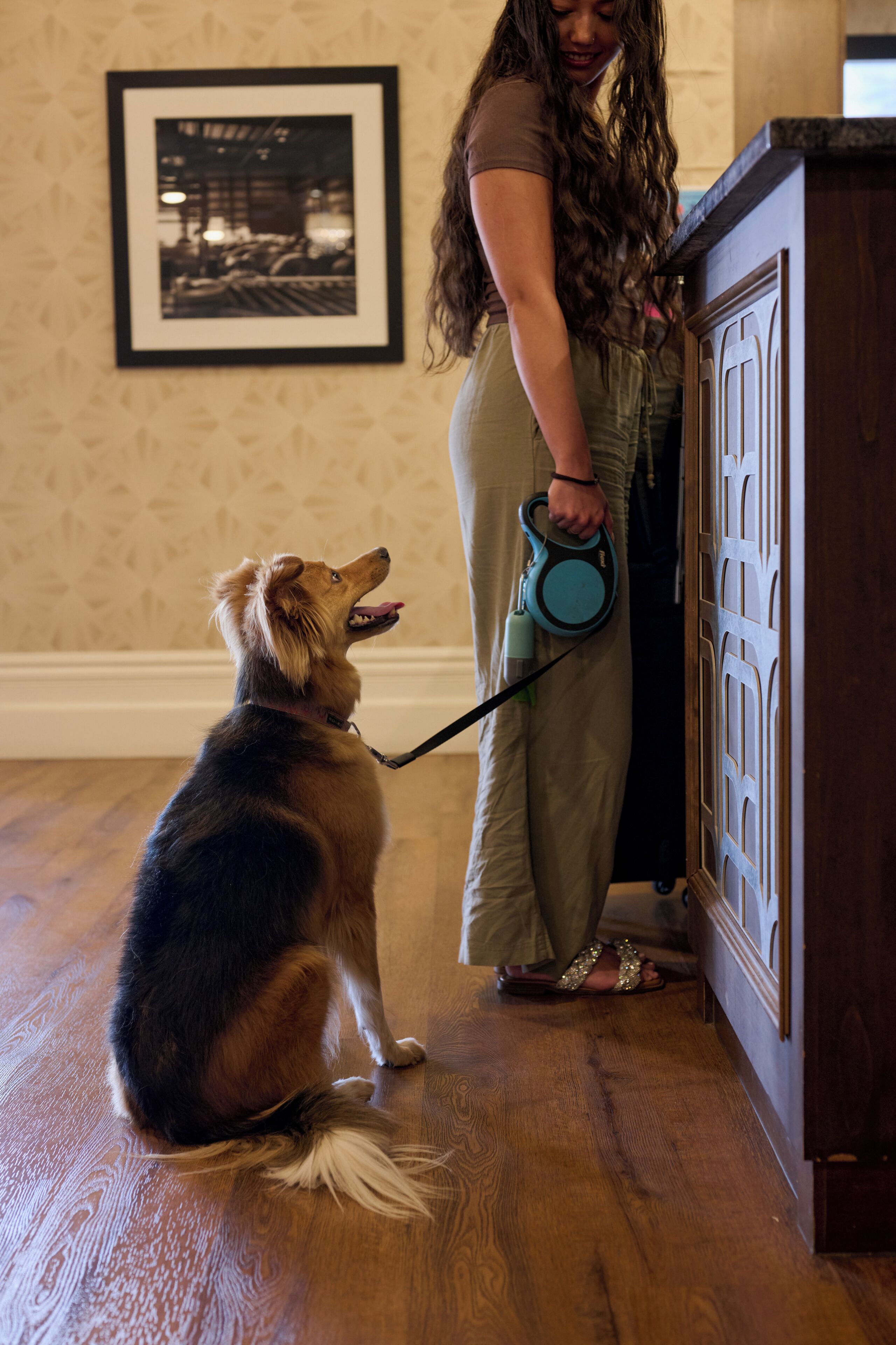 A person with a dog in a room with wooden flooring and a cabinet with a decorative door.