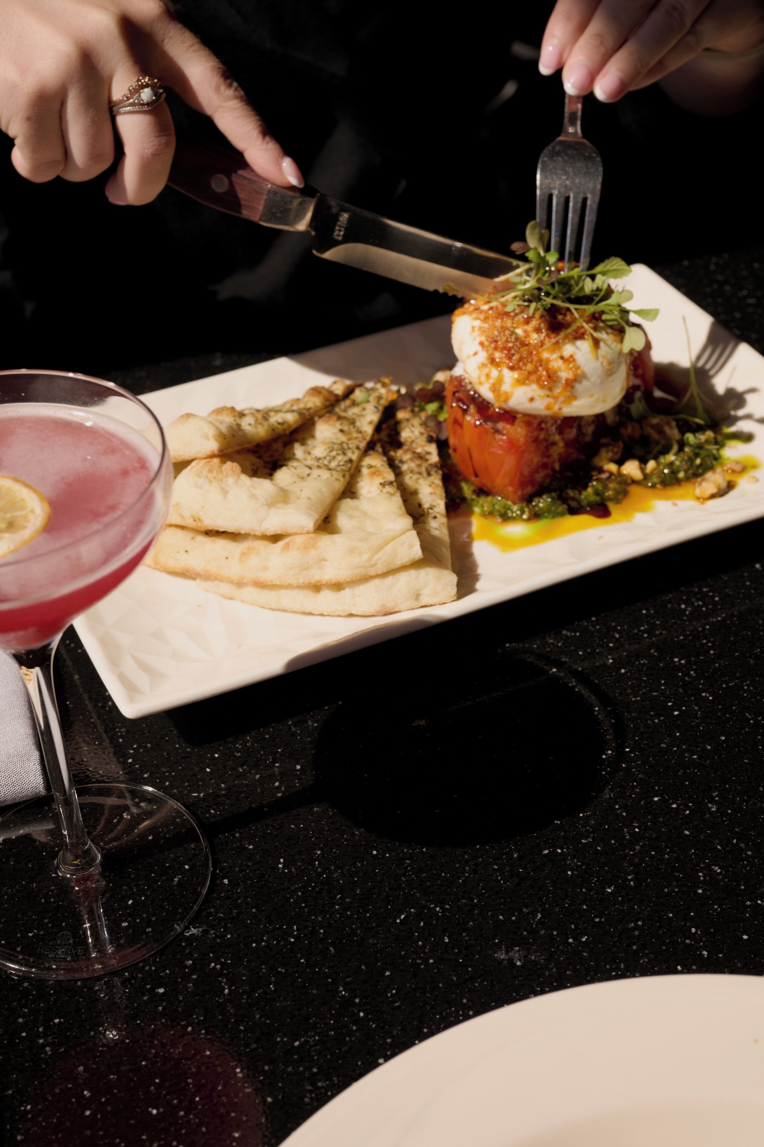 A dining table with a plate of food, a glass of red drink, and a fork.