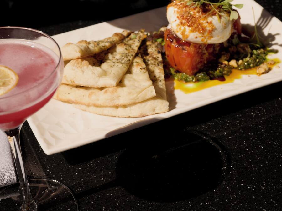 A dining table with a plate of food, a glass of red drink, and a fork.
