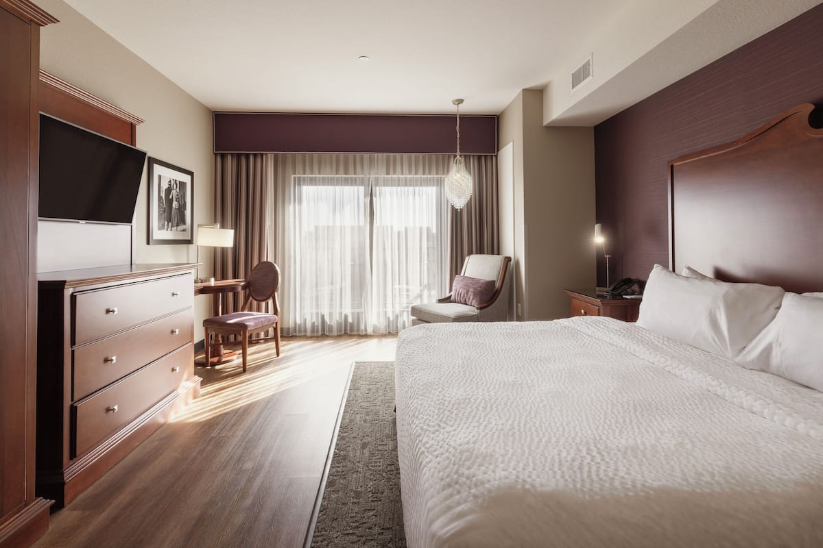 A hotel room with a large bed, a desk with a chair, a television, and a window with curtains.