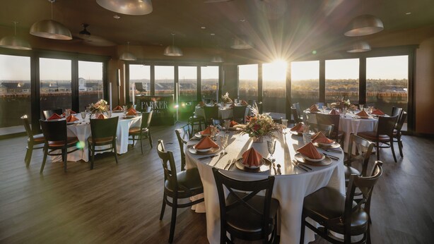 A restaurant with multiple tables set for dining, large windows offering a view of the city, and pendant lighting. - The Parker Hotel (Parker)