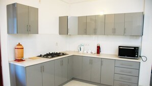 A kitchen with grey cabinets, a gas stove, a kettle, a microwave, and a red kettle on the countertop. - Niru Residence (Kandy)