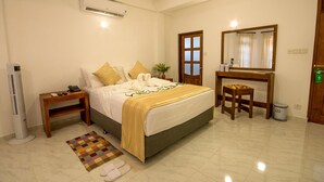 A hotel room with a bed, bedside table, a desk, a chair, a mirror, a waste bin, and a radiator. - Niru Residence (Kandy)