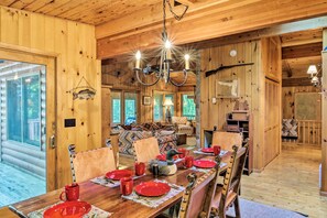 Een houten cabinestinterieur met een eettafel voor zes personen, een kroonluchter en een gezellig woongedeelte met een bank en open haard.