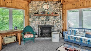 A cozy room with a stone fireplace, wooden ceiling, and large windows overlooking greenery. - Rustic Cozy Cabin on Island Lake w/ Fire Pit, Dock (Park Rapids)