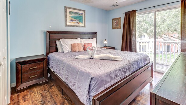 A bedroom with a large bed, a nightstand, a dresser, and a window with curtains. - Unit 15 | 3BR Home | 2 Mi to Disney | Pet Friendly | Heated Pool | Gated (Kissimmee)