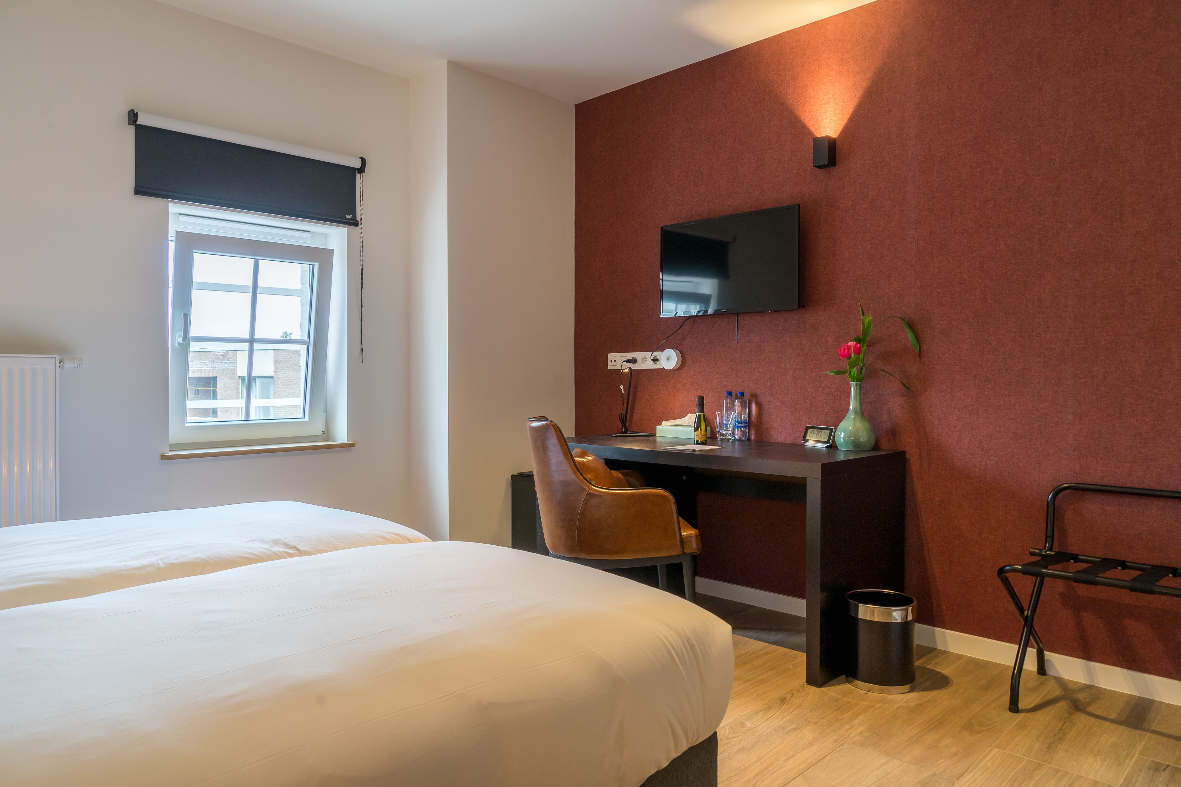 Quarto de hotel com cama, escrivaninha, cadeira, televisão e janela.