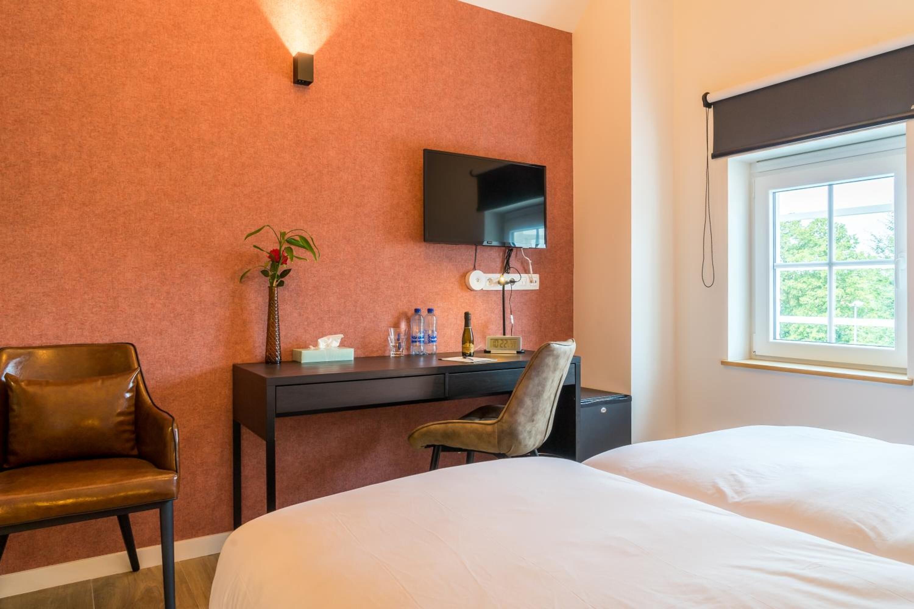 Ein Hotelzimmer mit Bett, Schreibtisch mit Fernseher, Stuhl, Pflanze und Fenster mit Blick.