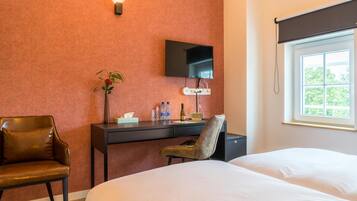 Ein Hotelzimmer mit Bett, Schreibtisch mit Fernseher, Stuhl, Pflanze und Fenster mit Blick.