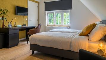 Un dormitorio con cama, mesita de noche y escritorio con silla. Se ve un ventanal con vistas a la vegetación.