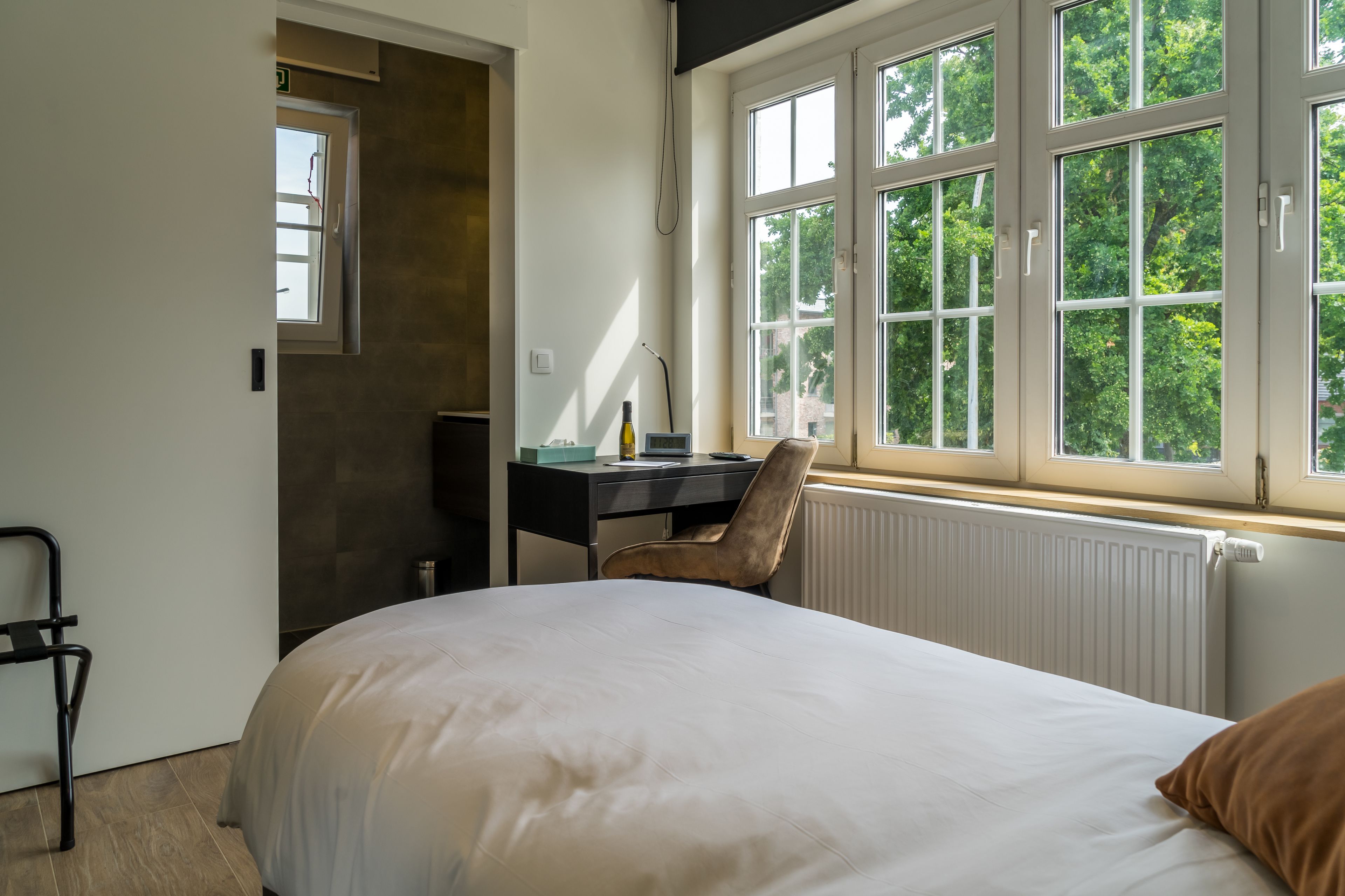 Un dormitorio con cama, escritorio, silla y ventana con vista a árboles.