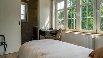 Un dormitorio con cama, escritorio, silla y ventana con vista a árboles.