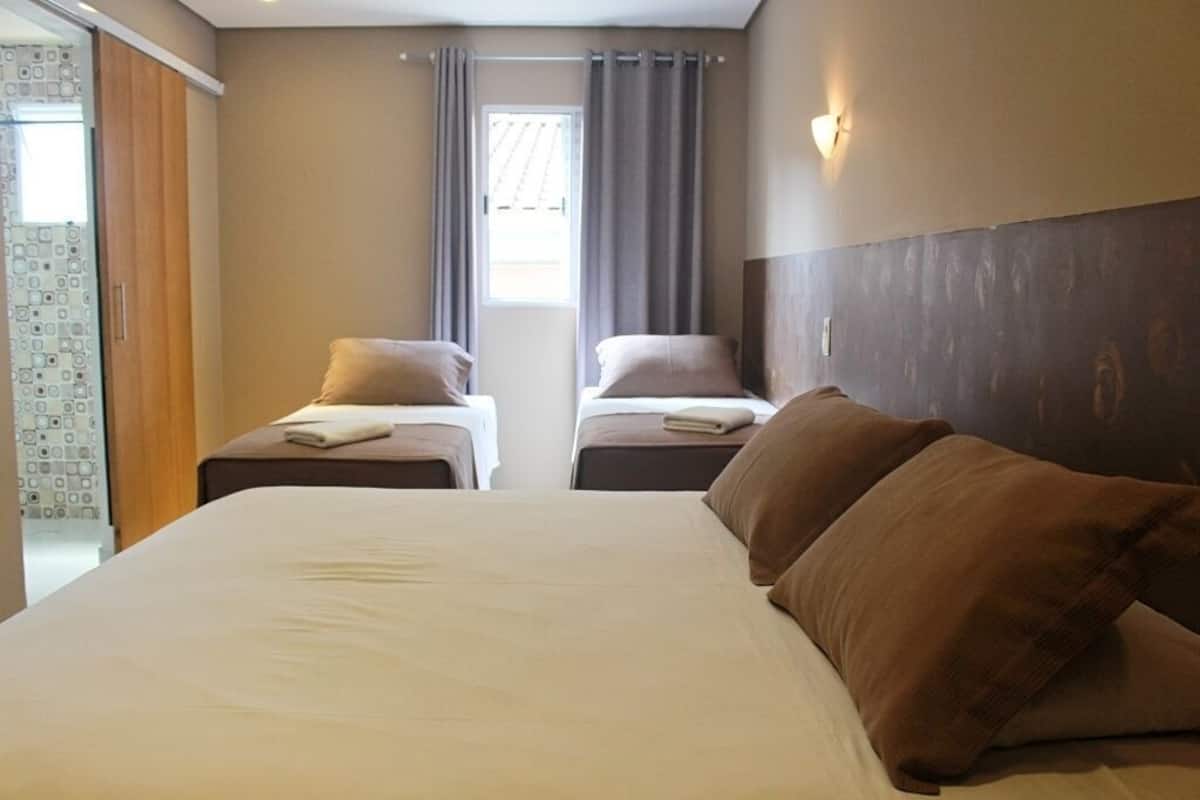 Une chambre d’hôtel avec deux lits, une grande fenêtre avec des rideaux et un luminaire fixé au mur.