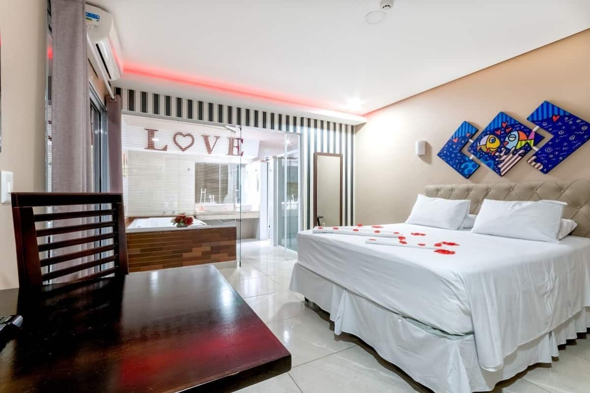 Une chambre d’hôtel avec un lit, une table en bois, un miroir et une fenêtre ornée d’un panneau indiquant le mot « AMOUR ».