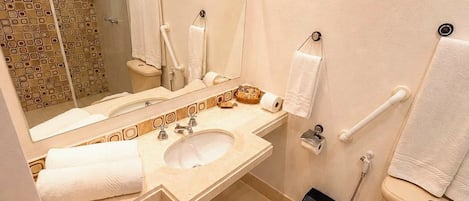 A bathroom with a sink, mirror, toilet, and shower area.