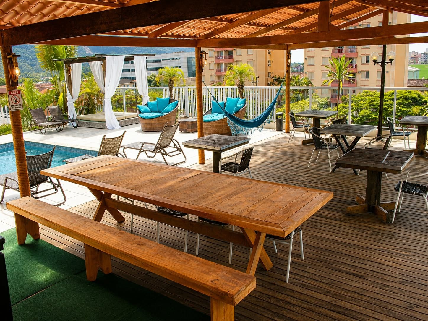 A covered outdoor area with wooden tables and benches, a pool, and lounge chairs.