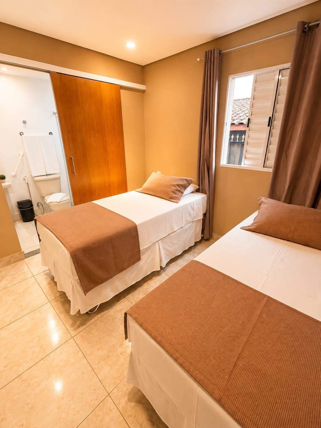 Habitación de hotel con dos camas, un baño y una ventana con cortinas.