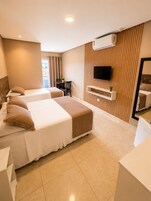 Une chambre d’hôtel avec deux lits, un téléviseur fixé à un mur en bois, une petite table avec une chaise et un appareil de climatisation.