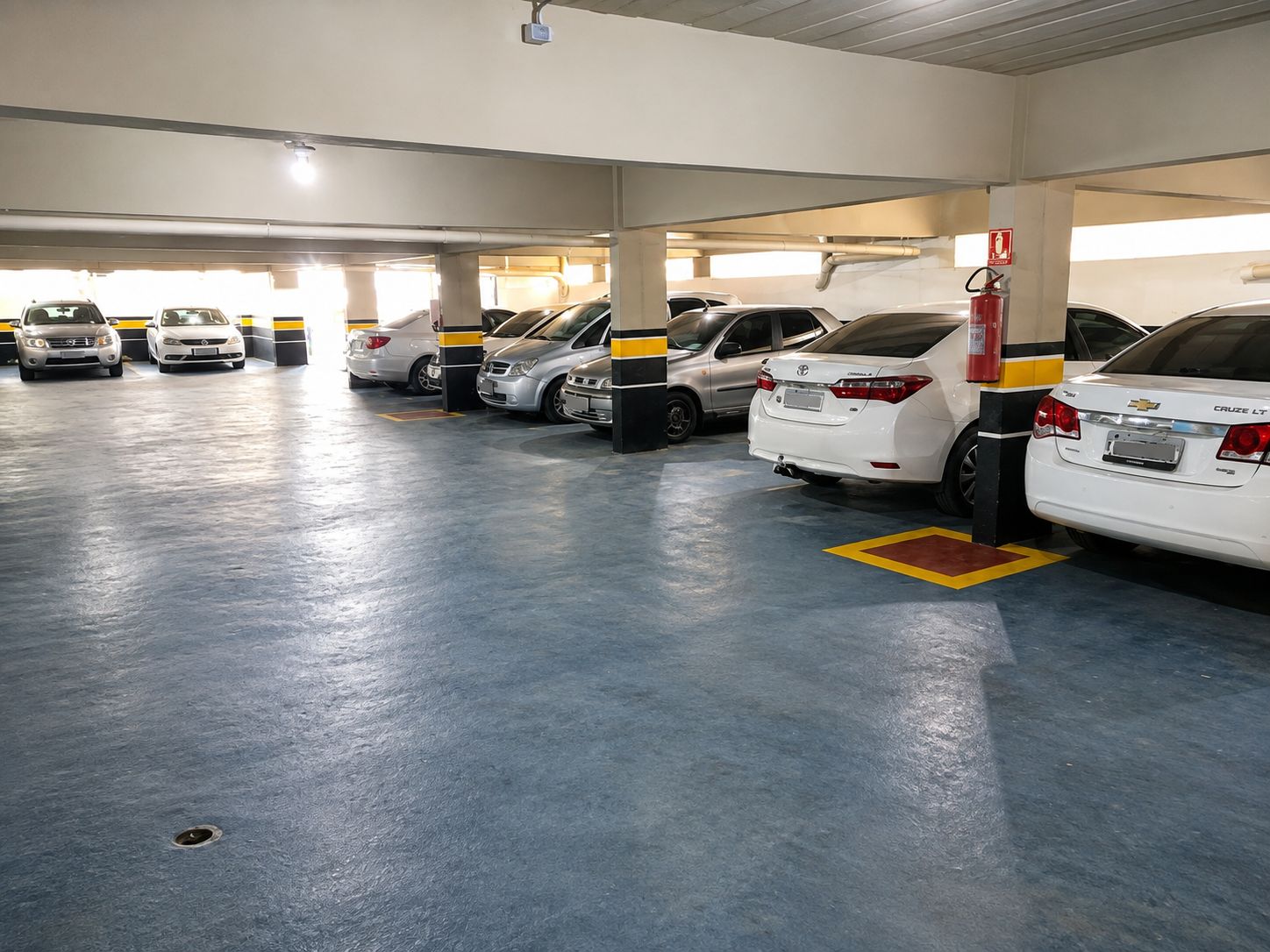 Un aparcamiento con varias filas de coches estacionados, extintores y una manguera contra incendios a la derecha.