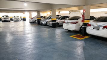 Un aparcamiento con varias filas de coches estacionados, extintores y una manguera contra incendios a la derecha.
